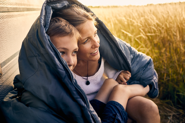 Mamma og gutt inntil campingvogn. Sitter i sovepose