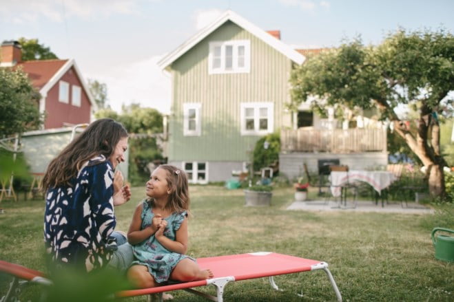 Mor og datter sitter på en solseng i en hage utenfor en hus